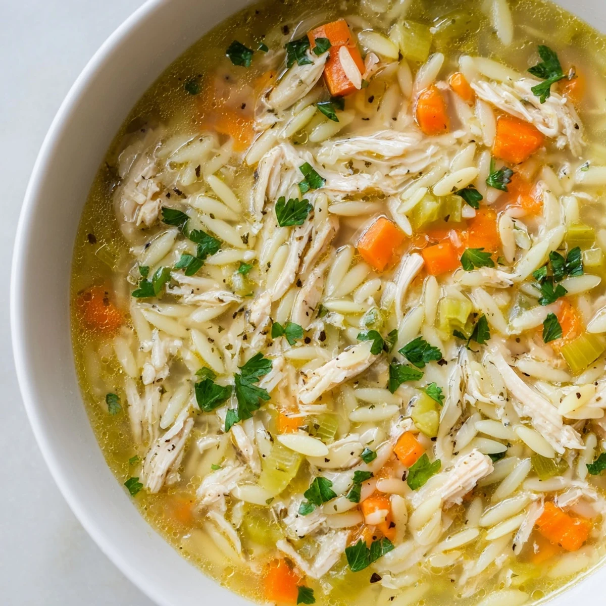 A steaming bowl of Lemon Pepper Chicken Orzo Soup, with tender shredded chicken and bright yellow lemon wedges garnishing the top.