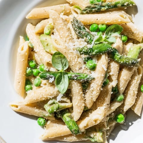Bright green asparagus, peas, and green beans mingle with penne in a creamy garlic Parmesan sauce, garnished with fresh basil.