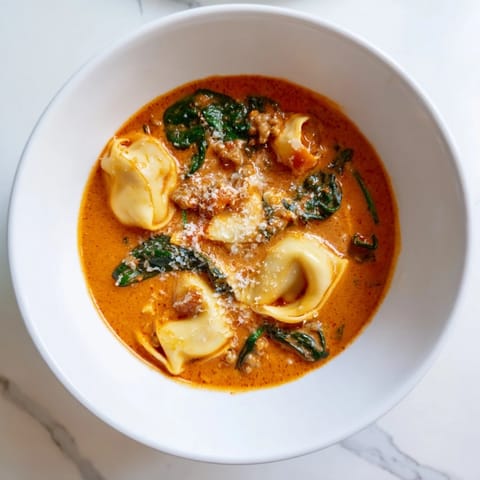 Comforting bowl of Tuscan Tortellini Soup topped with Parmesan, served with crusty bread.