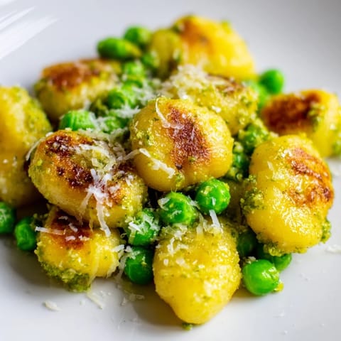 A close-up view of Pesto Pea Gnocchi Skillet, highlighting the steam rising from tender peas and golden potato dumplings.  